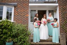 a group of women standing next to each other in front of a brick building holding bouquets