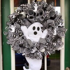 a wreath decorated with black and white striped ribbons, a ghost face on the front door