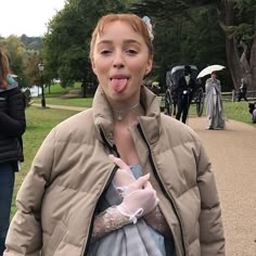 a woman sticking out her tongue while standing in a park with other people behind her