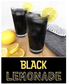 two glasses filled with black lemonade sitting on top of a wooden table next to sliced lemons