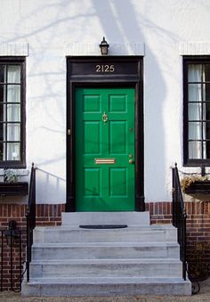 a green door is on the side of a white building with black windows and steps