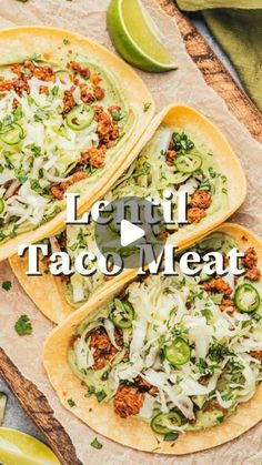 three tacos sitting on top of a wooden cutting board next to limes and cilantro