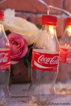 three coca - cola bottles sitting next to each other on a table with flowers in the background