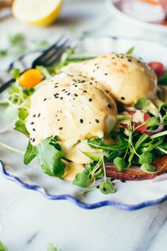 two buns with cheese on top of a salad in a plate next to a fork and knife