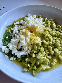 a white plate topped with broccoli and feta cheese covered in olive oil