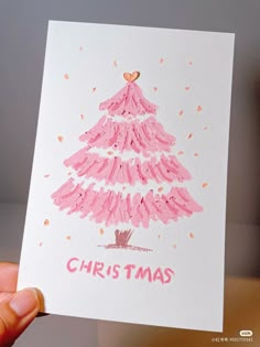 a hand holding up a card with a pink christmas tree on it's front