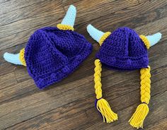 two crocheted hats with horns and braids on top of a wooden floor