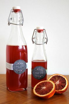 two bottles filled with blood orange juice next to sliced grapefruits on a wooden table