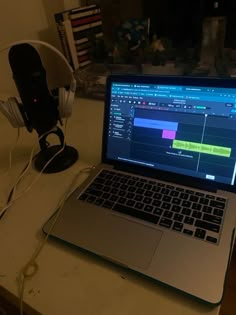 an open laptop computer sitting on top of a white desk next to headphones and a microphone