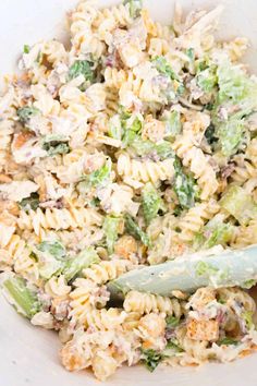 a pasta salad in a white bowl with a green serving utensil next to it