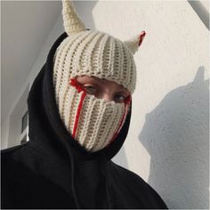 a person wearing a knitted mask with horns and fangs on their face, standing in front of a white wall