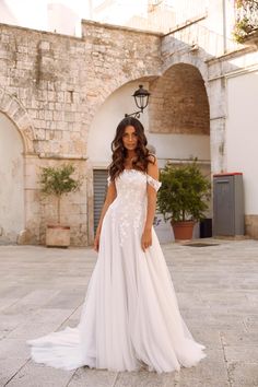 a woman wearing a white wedding dress standing in front of an old brick building with stone arches