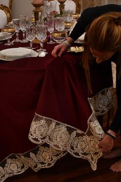 a woman is setting a table with red linens and white place mats on it