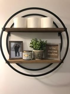 a circular shelf with two shelves holding toilet paper and some pictures on it next to a potted plant