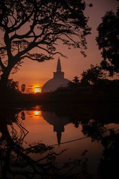 the sun is setting over a small lake in front of a church with a steeple