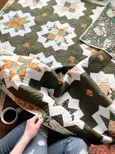 a woman is sitting on the floor next to some quilts and coffee mugs