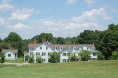 a large white house sitting in the middle of a lush green field next to trees