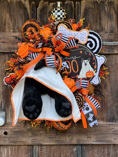 a halloween wreath with a teddy bear in the center and decorations around it on a wooden fence