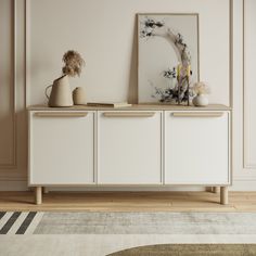 a white cabinet with two vases and a painting on the wall above it in a living room