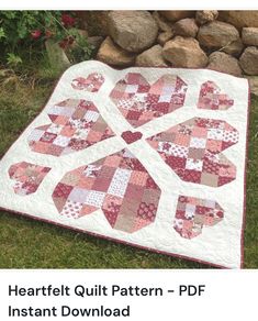 the heart quilt pattern is on display in front of some rocks and grass with flowers behind it