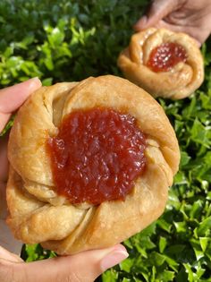 two small pastries with jam on them in front of some green bushes and grass