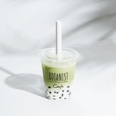 a green drink with a straw in it sitting on a white tableclothed surface