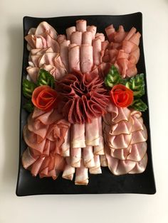 an arrangement of meats and vegetables on a black plate with red flowers in the center