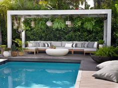 an outdoor living area with couches, tables and a swimming pool surrounded by greenery