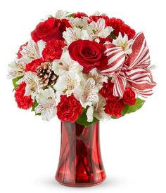 a red vase filled with white and red flowers on top of a wooden table next to a candy cane