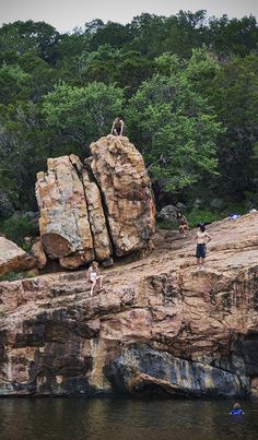 some people are standing on the rocks by the water and one person is swimming in the water