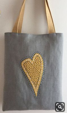 a gray bag with a yellow heart embroidered on the front and side, hanging from a hook