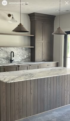 an empty kitchen with marble counter tops and wooden cabinetry, along with hanging lights