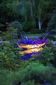 a boat that is sitting in the grass near some trees and water with lights on it