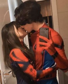 a man and woman in spiderman costumes are looking at their cell phones while standing next to each other