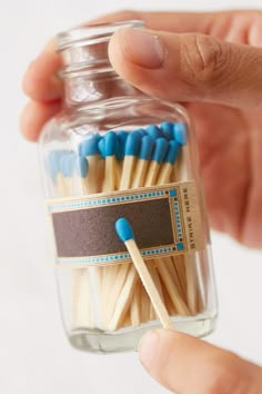 a hand holding a glass jar filled with matchsticks next to a person's finger