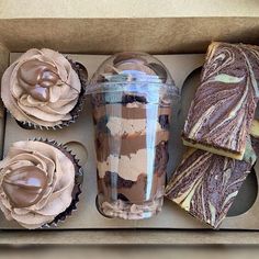 cupcakes in a box with chocolate frosting and two pieces of cake next to it