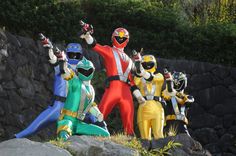 five people dressed as power rangers standing in front of some rocks and grass with their hands up