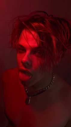 a shirtless man with red light on his face and neck chain around his neck