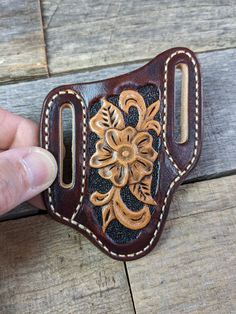 a handmade leather belt with flowers and leaves on the side, being held by a person's finger