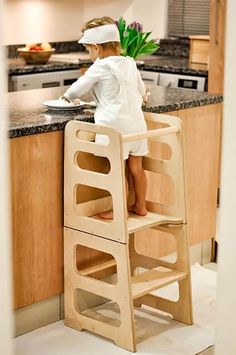 a young child sitting on top of a wooden step stool next to a kitchen counter