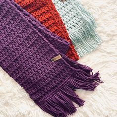 three different colors of knitted scarves laying on a white furnishing area