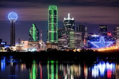 the city skyline is lit up at night with bright lights reflecting in the water below