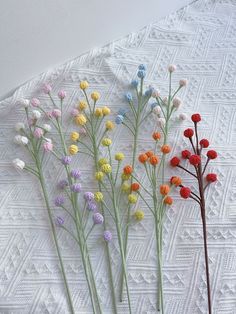 four different colored flowers are in a vase on a white lace tablecloth with geometric designs