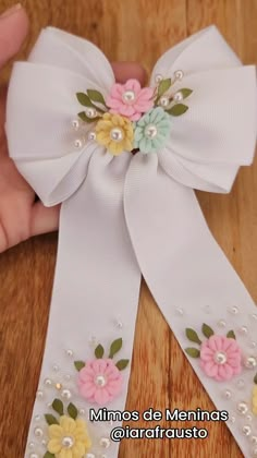 a hand holding a white ribbon with flowers and pearls on the side that is attached to a wooden table