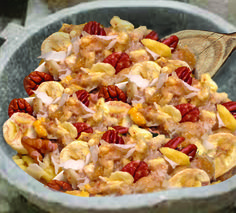 a bowl filled with fruit and nuts next to a wooden spoon