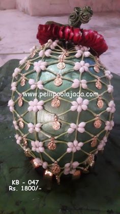 a green vase with white flowers and red ribbons on it's top sitting on a rock