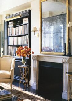 a living room filled with furniture and a large mirror above the fire place in front of a bookshelf