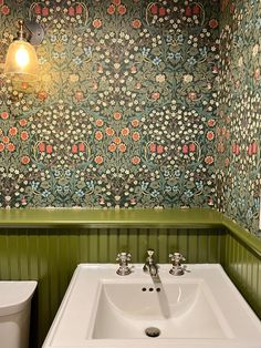 a bathroom with green walls and floral wallpaper on the walls, along with a white sink