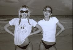 two women in bathing suits standing on the beach with their hands on their hipss