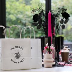 two white shopping bags sitting on top of a table next to candles and vases